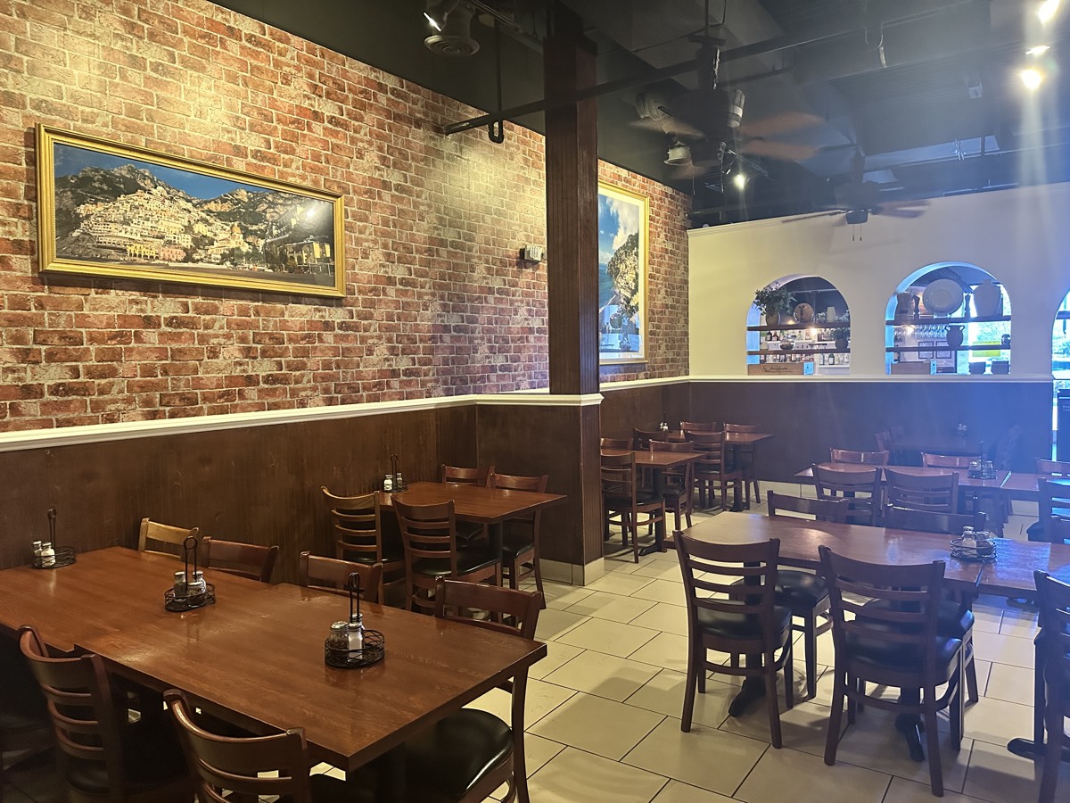 Capriccio dining room — exposed brick walls with Italian paintings and warm wood dining tables